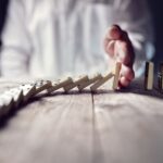 Domino effect in schedule management, man's hand interrupts falling domino pieces.